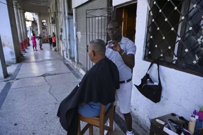 Um barbeiro corta o cabelo de um cliente do lado de fora de sua barbearia após um apagão em 5 de março de 2026