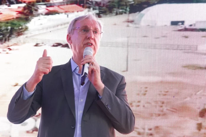 Celso Pansera é um homem alto, branco, de cabelos brancos e segura um microfone em cerimônia de abertura para apresentá-lo ao cargo de presidente da Codemar. Ao fundo está projetada uma imagem de obras.