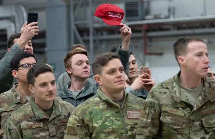 Membro das Forças Armadas dos EUA exibe um boné com o slogan "Make America Great Again" enquanto o presidente dos EUA, Donald Trump, e a primeira-dama, Melania Trump, cumprimentam militares americanos durante uma visita à Base Aérea de Ramstein, na Alemanha, em 27 de dezembro de 2018