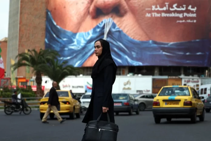 Mulher passa por um cartaz anti-EUA que faz referência ao presidente Donald Trump e ao Estreito de Ormuz, instalado em um prédio na Praça Valiasr, em Teerã, em 2 de maio de 2026